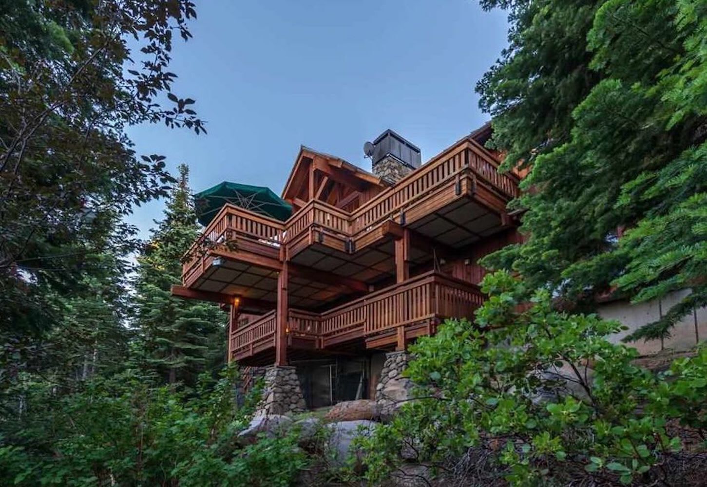 A multi-level wooden cabin with balconies, surrounded by dense forest.