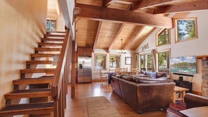A spacious living area with a wooden staircase, a large leather sofa, and a television. - Northstar Treehouse – Chic 4BR House | Forest view in Northstar Ski Resort (Truckee)