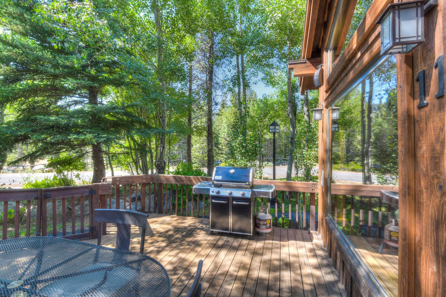 Une terrasse en bois avec un barbecue et une table, entourée d’arbres.