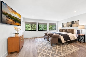Un dormitorio moderno con una cama grande, dos sillones, un aparador de madera y un cuadro de un paisaje.