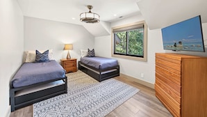 Une chambre avec deux lits, une commode en bois, une télévision et une fenêtre donnant sur les arbres et le ciel.