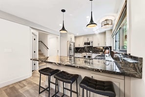 A modern kitchen with a marble countertop, stainless steel appliances, and black bar stools. - The Seasons - Tahoe - 4BDR Cabin (Tahoe Vista)