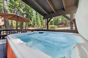 Un jacuzzi bajo una pérgola de madera con vistas a un bosque.