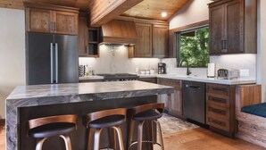 A modern kitchen with a large island, wooden cabinets, and a view of greenery outside. - Shoreline Vista | 180° Lake Views | Pet-Friendly | 2 Master Suites (Carnelian Bay)