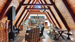 A cozy attic living room with a fireplace, wooden beams, and a large window overlooking a deck.