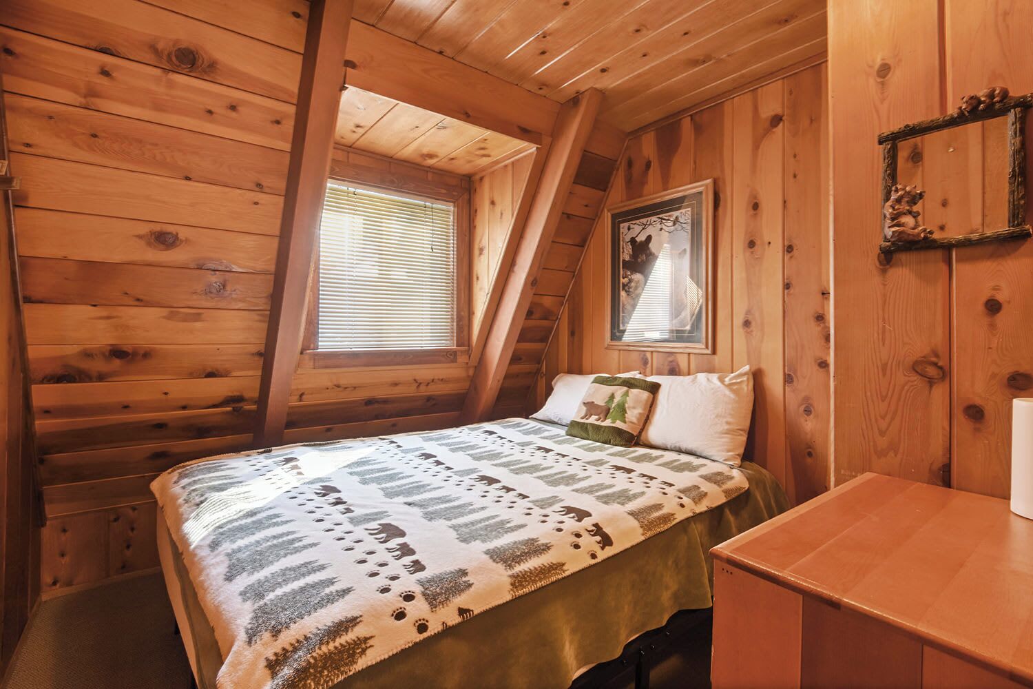 A cozy cabin room with a bed, a small desk, and a window with blinds.