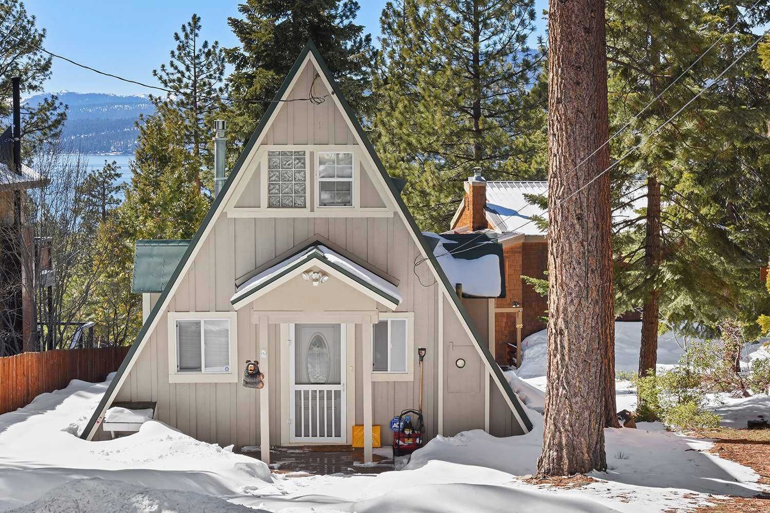 Una cabaña pequeña y triangular con un porche delantero y una chimenea, rodeada de nieve y árboles.