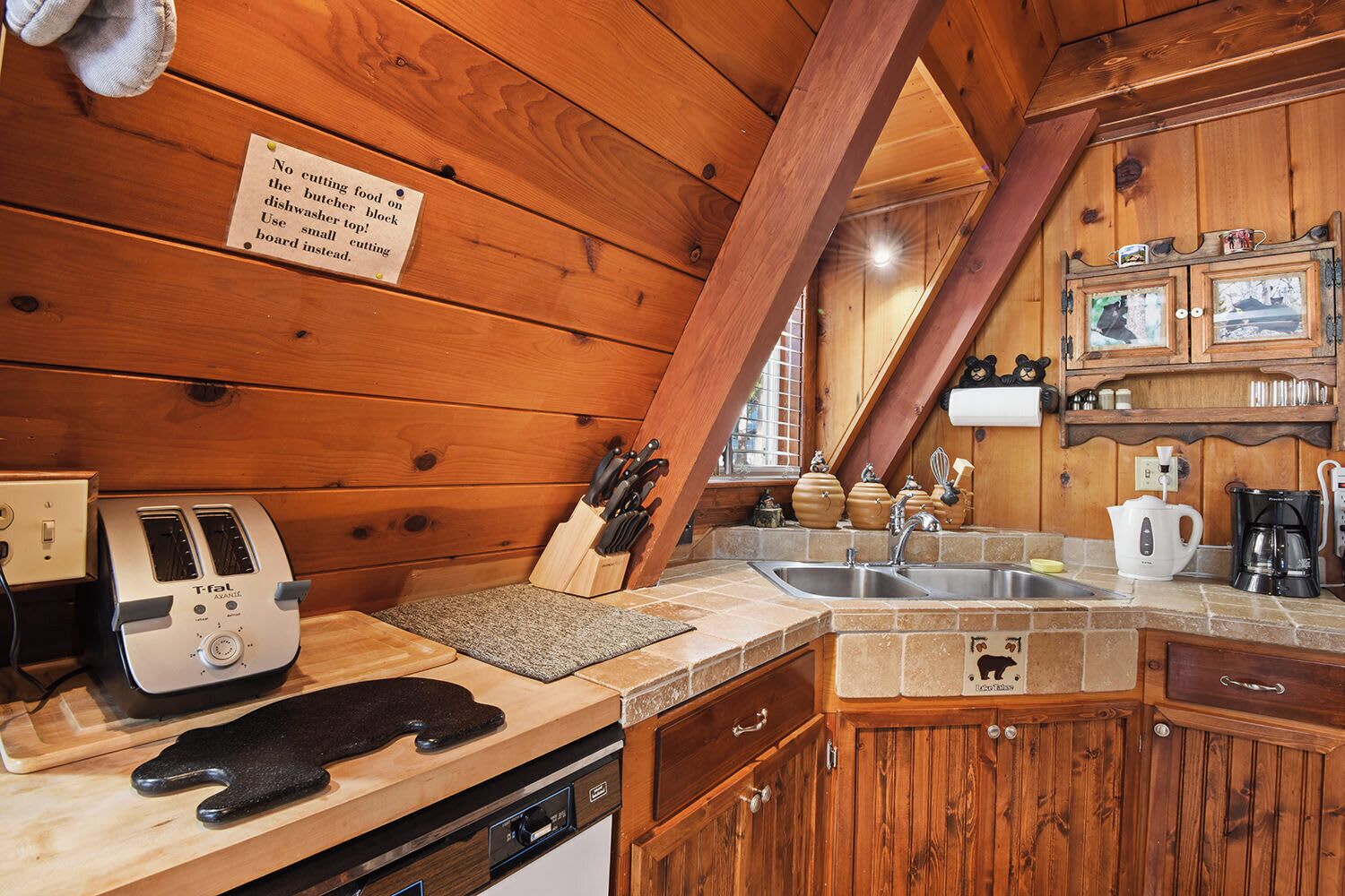 A cozy kitchen with wooden walls, a two-burner stove, a sink, and a toaster.