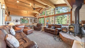 Un salon chaleureux avec des canapés en cuir, une cheminée et de grandes fenêtres donnant sur une forêt.