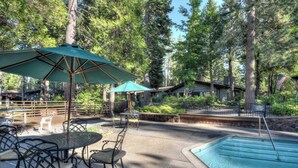 An outdoor pool area with a table and chairs, surrounded by trees and a wooden building.