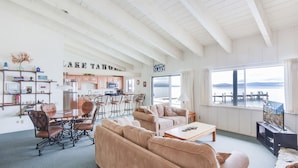 A spacious living room with a large window overlooking a lake, a kitchen area, and a cozy seating arrangement.