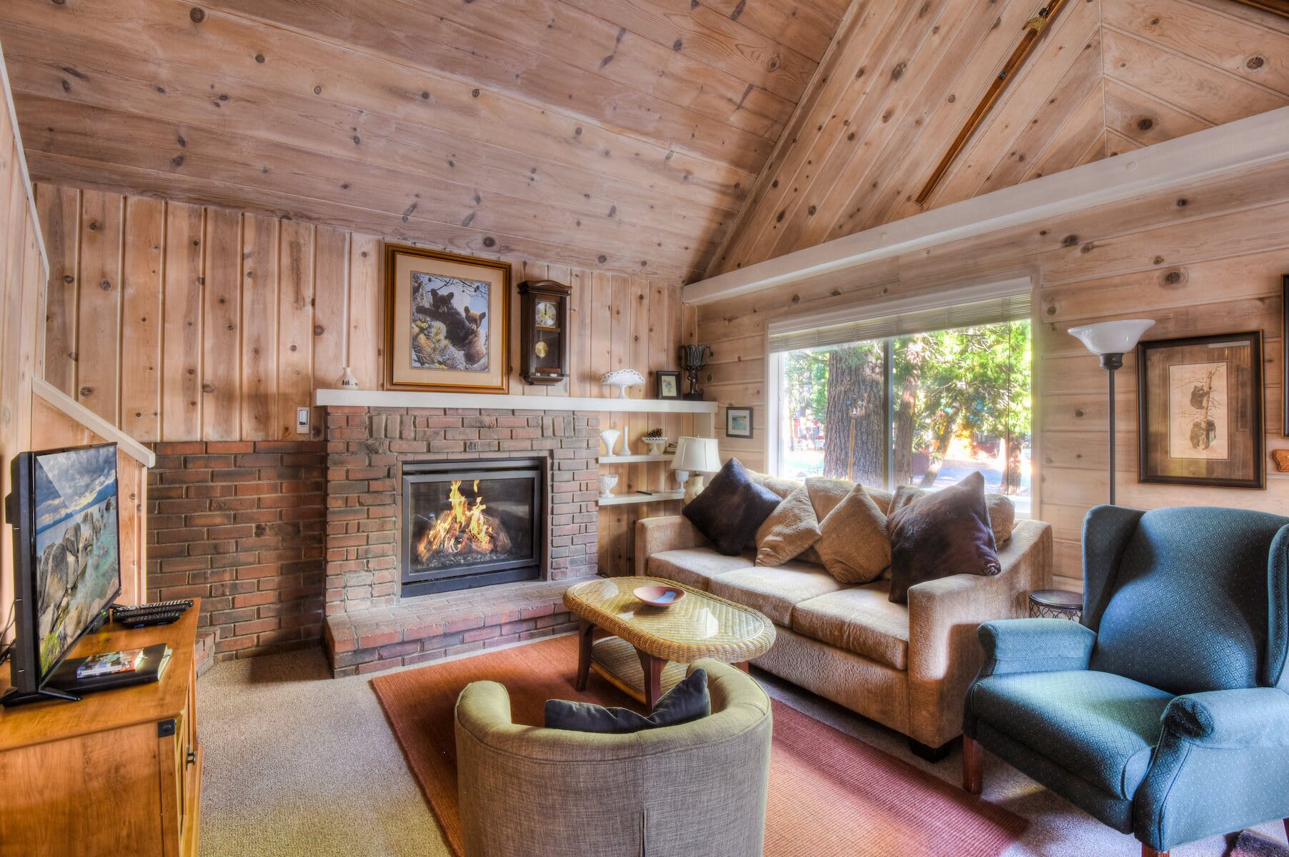Ein gemütliches Blockhaus-Interieur mit Kamin, Holzwänden, einer Couch und einem Fernseher.