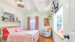 Une chambre à coucher avec un lit, une fenêtre avec des rideaux, un téléviseur fixé au mur et un ventilateur de plafond.