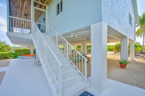 Une maison à deux étages, avec une façade blanche, un porche et un escalier menant à l’étage supérieur.