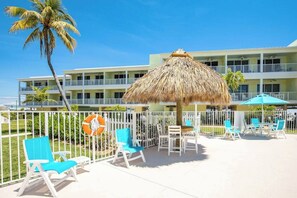 A resort with a thatched umbrella, white railings, and blue lounge chairs. - *NEW* Finer Things-Beach/Pool (Key Colony Beach)