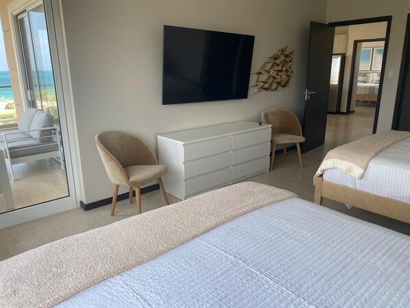 A modern bedroom with a large bed, a TV mounted on the wall, a white dresser, and a chair. - FABULOUS BEACH & POOL VIEWS IN THIS STUNNING 2 BDRM CORNER UNIT AT LE VENT (Eagle Beach)
