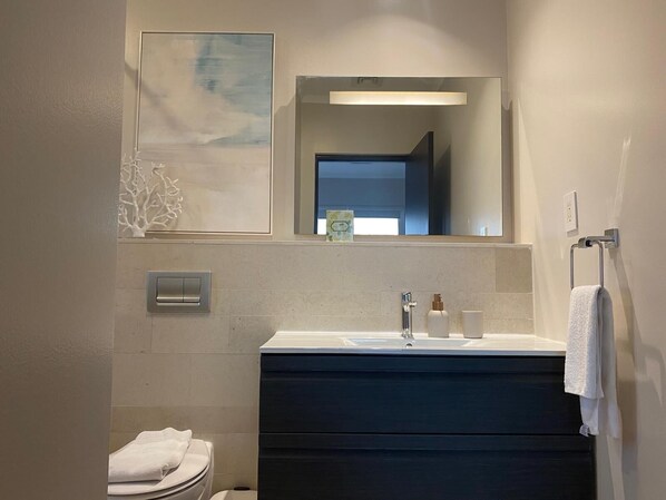 Un baño moderno con lavamanos blanco, tocador oscuro y un espejo grande.
