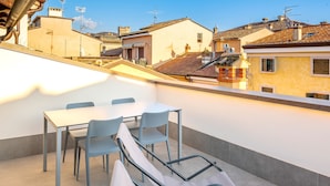 Eine Dachterrasse mit Tisch, Stühlen, Sonnenschirm und Blick auf die umliegenden Gebäude.