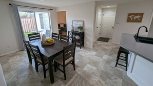Una cucina moderna con zona pranzo, caratterizzata da un tavolo grande e sedie, lavello incassato e vista sul giardino attraverso una porta scorrevole in vetro.