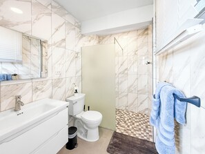 Un baño con lavamanos, inodoro y zona de ducha blanca.