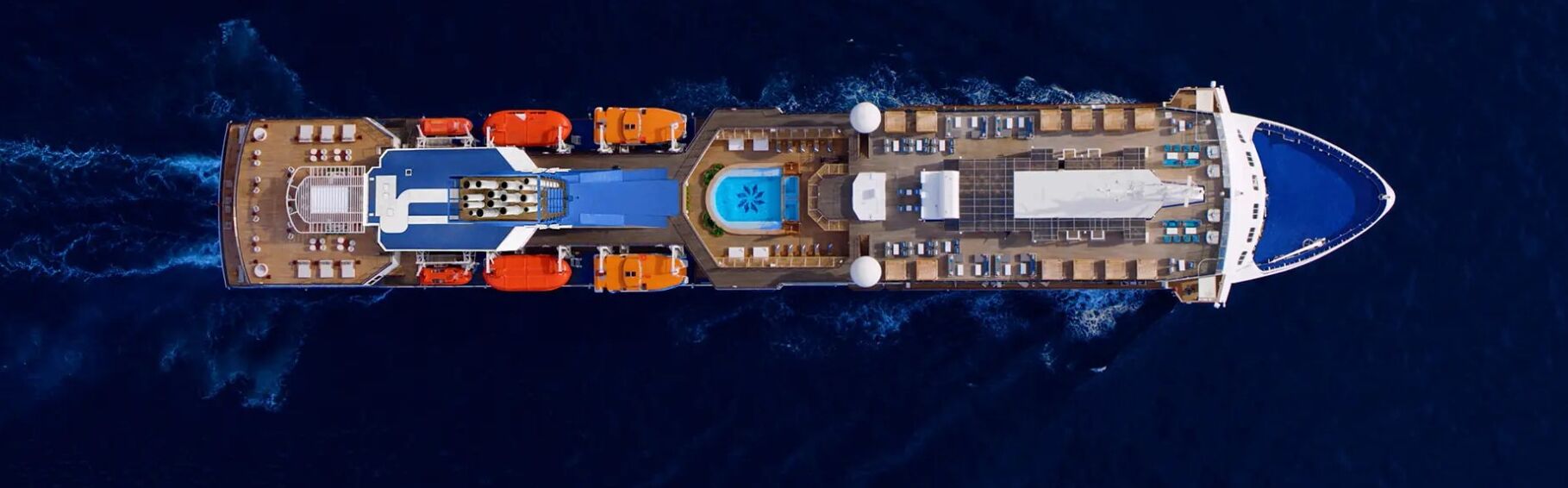 Een groot cruiseschip met meerdere dekken, waaronder een zwembad, ligbedden en een centraal gelegen eetruimte.