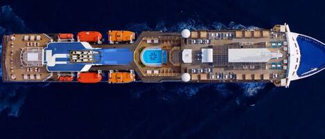 Een groot cruiseschip met meerdere dekken, waaronder een zwembad, ligbedden en een centraal gelegen eetruimte.