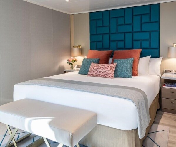 Une chambre d’hôtel moderne avec un grand lit, une banquette, une table de chevet et un mur orné d’un motif géométrique.