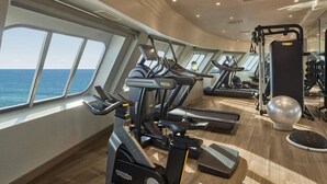 A gym with treadmills, a weight machine, and a rowing machine, with large windows overlooking the ocean.
