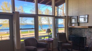 Una habitación acogedora con chimenea, un ventanal con vistas al lago y una zona de estar con dos sillones.