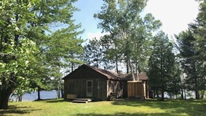 Eine Holzhütte mit Veranda, umgeben von Bäumen und einem See.
