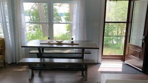 Ein Zimmer mit Picknicktisch, einer zur Außenseite führenden Tür und Blick auf Bäume durch die Fenster.