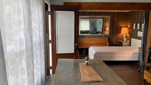 Ein Hotelzimmer mit Holztisch, einer weißen Bank, einem Bett, einer Couch und einer kleinen Küchenzeile.