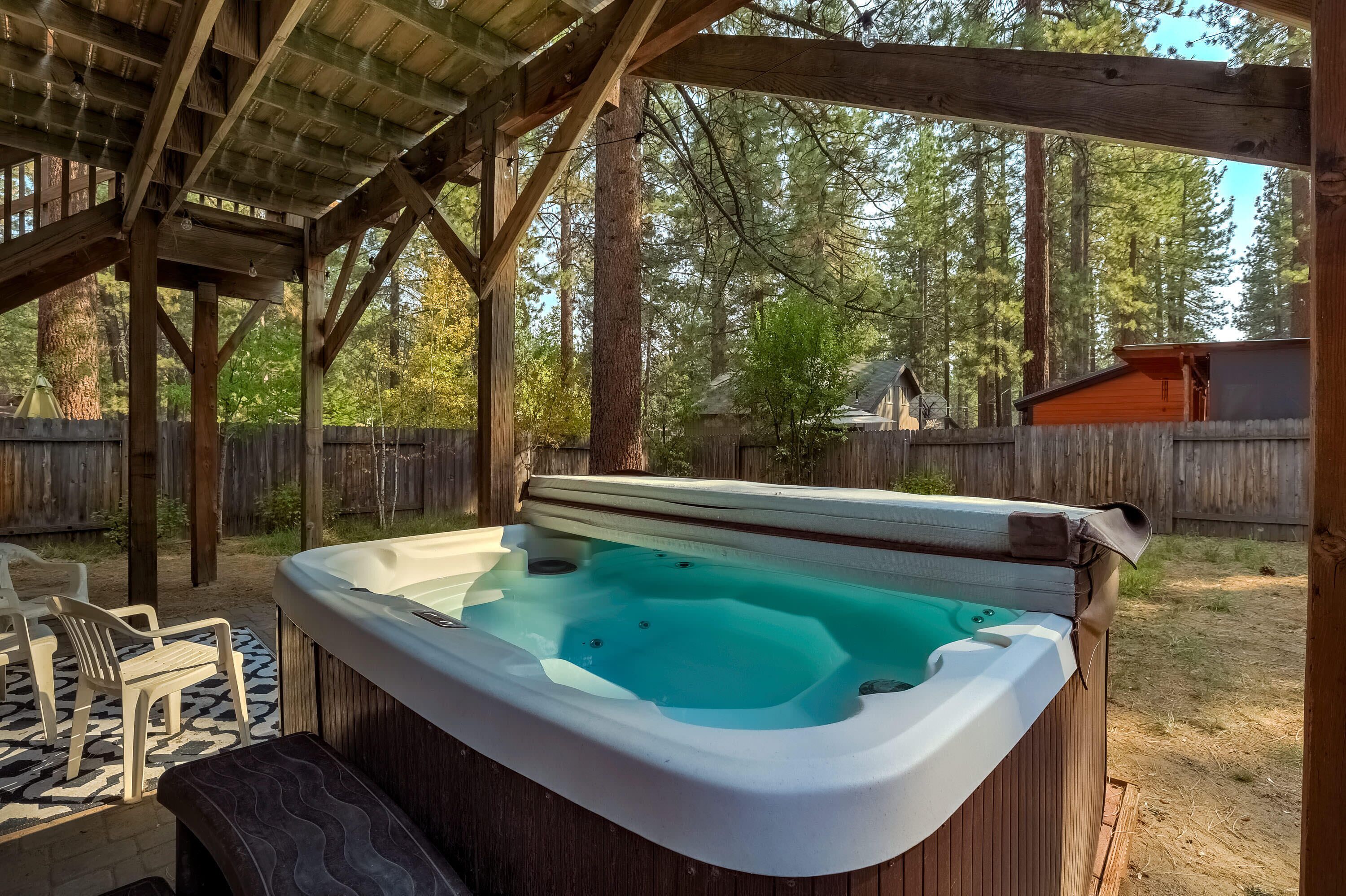 Un bain à remous sous une pergola en bois, avec une clôture en bois et des arbres en arrière-plan.