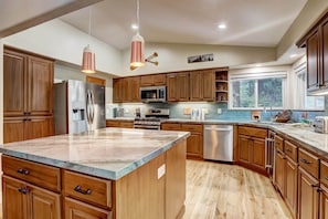 Una cucina moderna con mobili in legno, elettrodomestici in acciaio inossidabile, una grande isola e illuminazione a sospensione.