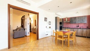 A modern kitchen with a red-tiled backsplash, wooden cabinets, and a dining area with a table and chairs. - LuminArt (Gibellina)