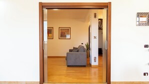 A room with a wooden-framed sliding door, a grey sofa, and a potted plant. - LuminArt (Gibellina)
