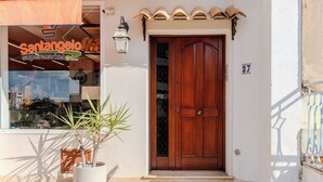 A storefront with a wooden door and a potted plant in front. - LuminArt (Gibellina)