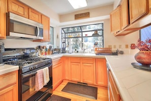 A kitchen with wooden cabinets, a microwave, stove, and a large window.