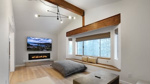 Una sala de estar moderna con chimenea, un televisor grande y un ventanal con vistas a árboles.
