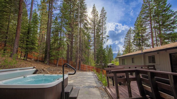 Un jacuzzi, una terraza de madera y una cabaña en un bosque.