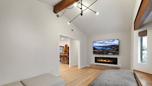 Un dormitorio moderno con un amplio ventanal, chimenea y televisor montado en la pared.