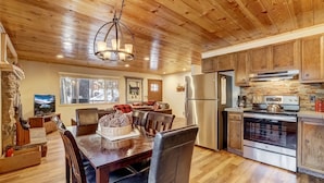 Una cocina con paneles de madera, comedor, chimenea de piedra y ventanas amplias.