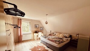 Un dormitorio con cama, escritorio, silla, radiador, ventana y alfombra de piel de vaca.