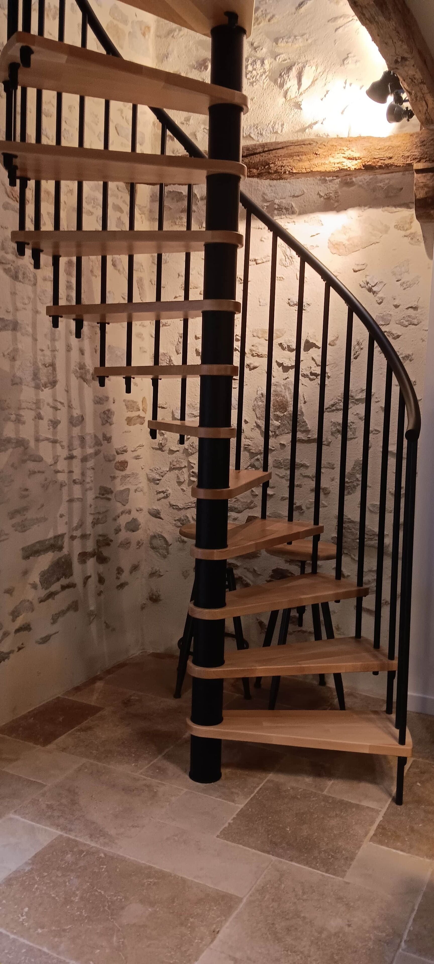 Un escalier en colimaçon avec des marches en bois et des rampes en métal noir, menant à l’étage supérieur.