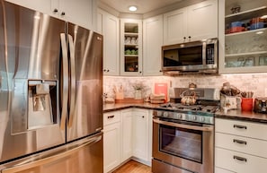 A modern kitchen with stainless steel appliances, white cabinetry, a built-in microwave, and a brick backsplash. - Serenity Woods - Game Room & More! (South Lake Tahoe)