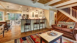 Un vaste espace de vie doté d’un plafond en bois, une cuisine avec un bar et un coin salon confortable avec un canapé et une table basse.