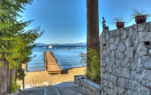 Un sentier en bois mène à une plage bordée d’un muret et agrémentée de plantes en pot.