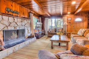 Interior acogedor de una cabaña con chimenea de piedra, paredes de madera, un sofá y un televisor.