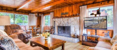 L’intérieur d’un chalet accueillant, avec une cheminée en pierre, des meubles en bois et un téléviseur.