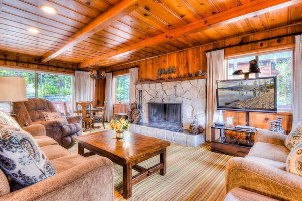 A cozy cabin interior with a stone fireplace, wooden furniture, and a television.